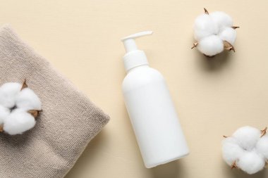 Düz kompozisyon, sıvı sabun, pamuk çiçekleri ve bej arka planda havlu.