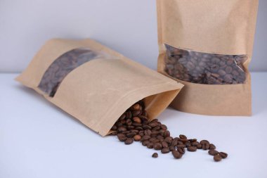 Açık gri arka planda kahve çekirdekli fermuar stand-up torbaları, yakın plan. Tasarım için model