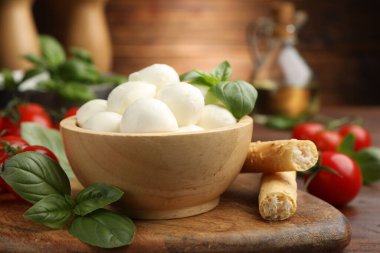 Lezzetli mozzarella peynir topları, ekmek çubukları, domates ve fesleğen ahşap masada, yakın plan.