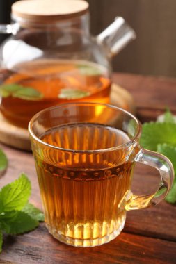 Cam fincanda aromatik limon merhemi çayı, çaydanlık ve ahşap masada taze yapraklar, yakın plan.