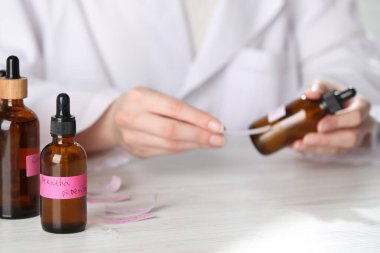 Laboratuvarda beyaz ahşap masada lüks parfüm üreten profesyonel bir parfümcü.