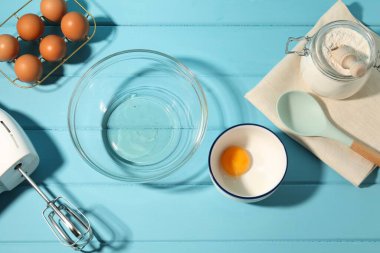 Krem şanti yapıyorum. Kase, el çırpıcı ve malzemeler açık mavi ahşap masada, düz yerde.