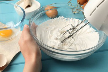 Açık mavi ahşap masada el çırpıcı kremalı bir kadın, yakın plan.