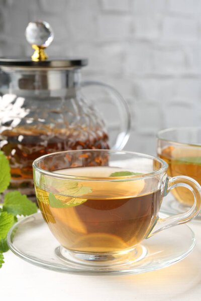 Ароматический лимонный бальзам чай в стеклянных чашках, чайник и свежие листья на белом столе, крупным планом
