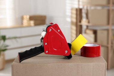 Kapalı alandaki karton kutunun üzerinde yapışkan bant ruloları olan bir dağıtıcı.