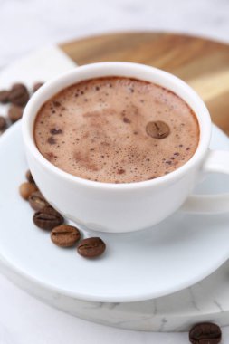 Aromatik kahve fincanda, fasulye ve çay tabağı beyaz masada, yakın plan.