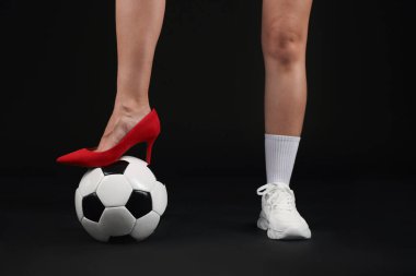 Arka planda futbol topu olan yüksek topuklu ayakkabılı ve spor ayakkabılı bir kadın.