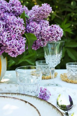 Güzel leylak çiçekleri, tabaklar, kaşık, bardaklar ve mumlar bahçede, yakın plan
