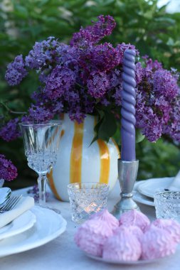Güzel leylak çiçekleri, zephyrler, tabaklar, çatal bıçak takımı, cam ve mumlar bahçede, yakın plan