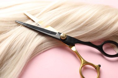 Açık pembe arka planda saç teli ve makas, yakın plan.