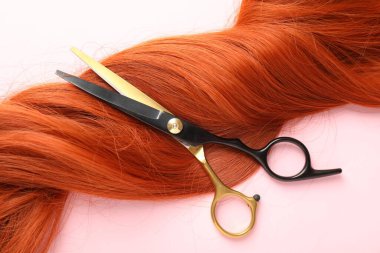 Açık pembe zemin üzerinde saç teli ve makas, üst görünüm