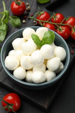 Lezzetli mozzarella peynir topları kasede, fesleğende, biberlikte ve domateslerde siyah masada, yukarıda.