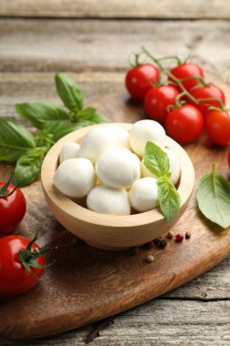 Lezzetli mozzarella peynir topları kasede, fesleğende, biberlikte ve domateslerde ahşap masada, yakın planda.