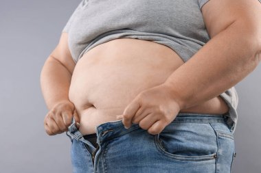 Kilolu kadın gri arka planda dar kot pantolon giymeye çalışıyor, yakın plan.