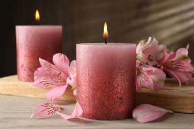 Beyaz ahşap masada yanan mumlar ve zambak çiçekleri, yakın plan.