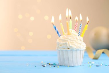 Kekin içinde mumlar yakmak, süslemeler ve açık mavi masa üzerinde parti dekorasyonu bej arka planda bulanık ışıklar, metin için boşluk