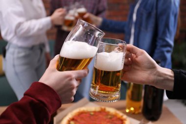 Arkadaşlar masada bira bardaklarını tokuşturur, yakın plan