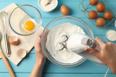 Açık mavi ahşap masada el çırpıcı kremalı bir kadın.