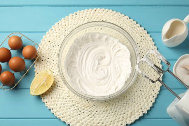 Açık mavi ahşap masa üzerinde çırpılmış krema, yumurta ve diğer ürünlerle el çırpıcı düz yatıyordu.
