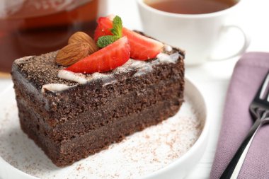 Çilekli, bademli ve masada çay bulunan bir dilim lezzetli çikolatalı pasta.