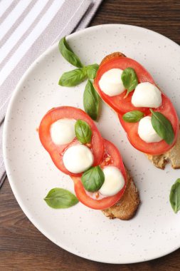 Peynirli, domatesli, ahşap masadaki fesleğenli lezzetli sandviçler.