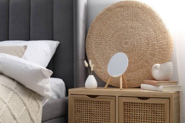 Yatağın yanında ayna, dekor ve kitap olan bir komodin.