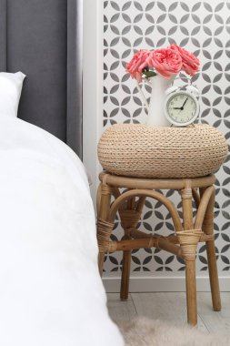 Çalar saati olan yan masa ve yatağın yanında çiçekler.