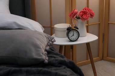 Çalar saati olan yan masa ve yatağın yanındaki dekor.