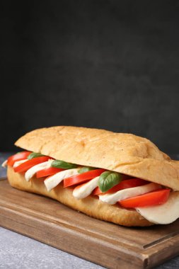 Mozarella peynirli, domatesli ve fesleğenli lezzetli sandviç. Gri desenli masa, koyu arkaplanlı, yakın plan.