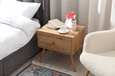 İçinde kahve, kitap ve yatağın yanında dekor olan komodin.