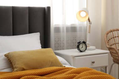 Yatağın yanında lamba ve çalar saat olan komodinin yanında.