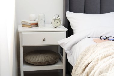 Yatağın yanında alarm saati ve dekorasyonu olan komodinin yanında.