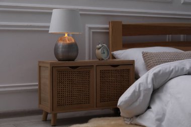 Yatağın yanında lamba ve çalar saat olan komodinin yanında.