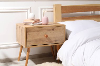 Yatağın yanında kitap ve dekor olan bir komodin.