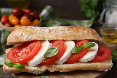 Mozarella peynirli, domatesli ve ahşap masadaki fesleğenli lezzetli sandviç.