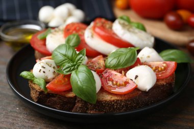 Peynirli, domatesli, fesleğenli ve baharatlı lezzetli sandviçler ahşap masada, yakın plan.
