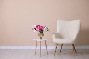 Bej duvarın yanında vazo dolusu çiçekli rahat koltuk ve masa, metin için yer