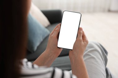 Evdeki koltukta modern akıllı telefon kullanan bir kadın.