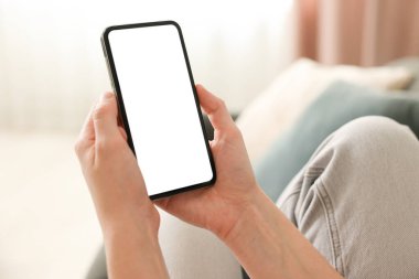 Evdeki koltukta modern akıllı telefon kullanan bir kadın.