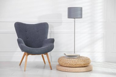 Rahat gri koltuk, lamba ve beyaz duvarın yanındaki kitaplar.