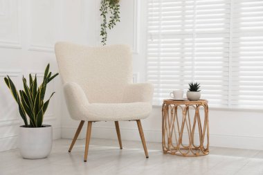 Rahat koltuk, yan masa ve beyaz duvarın yanındaki bitkiler.