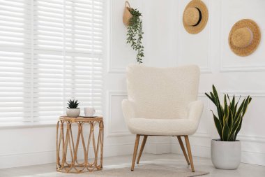 Rahat koltuk, yan masa ve beyaz duvarın yanındaki bitkiler.