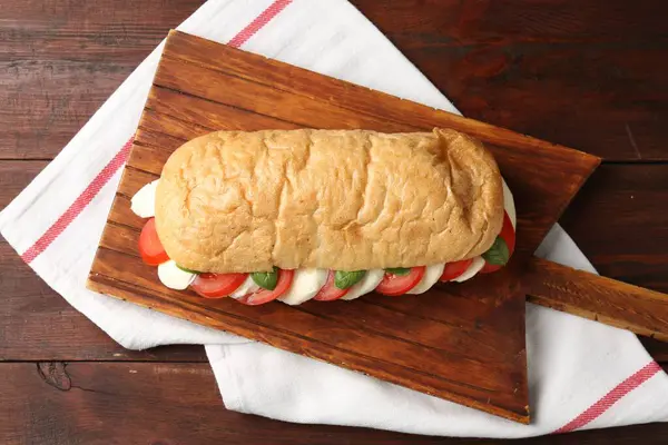 Peynirli, domatesli, ahşap masadaki fesleğenli lezzetli sandviç.