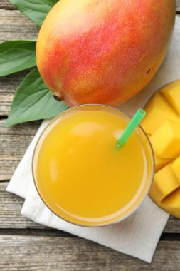 Lezzetli mango suyu bardakta, taze meyve ve yeşil yapraklar ahşap masada, düz yerde.