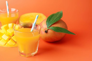 Bardakta lezzetli mango suyu ve turuncu arka planda taze meyve, yakın plan. Metin için boşluk