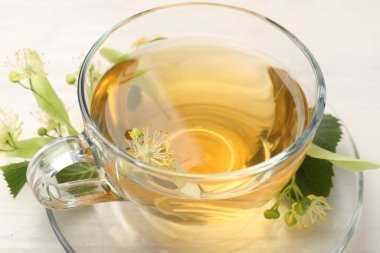 Fincanda taze ıhlamur çayı ve beyaz ahşap masada çiçekler, yakın plan.