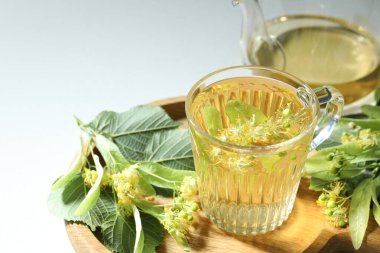 Fincanda lezzetli ıhlamur çayı, ışık masasında yapraklar ve çiçekler, yakın plan.