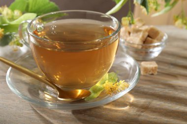 Lezzetli ıhlamur çayı, kaşık, yapraklar ve çiçekler ahşap masada, yakın plan.