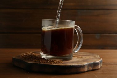 Bardağa sıcak su dökerek, hazır kahveyle ahşap masaya, yakın çekim.