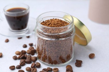 Cam kavanozdaki anlık kahve, fasulye ve sıcak içecek açık gri masada, yakın plan.